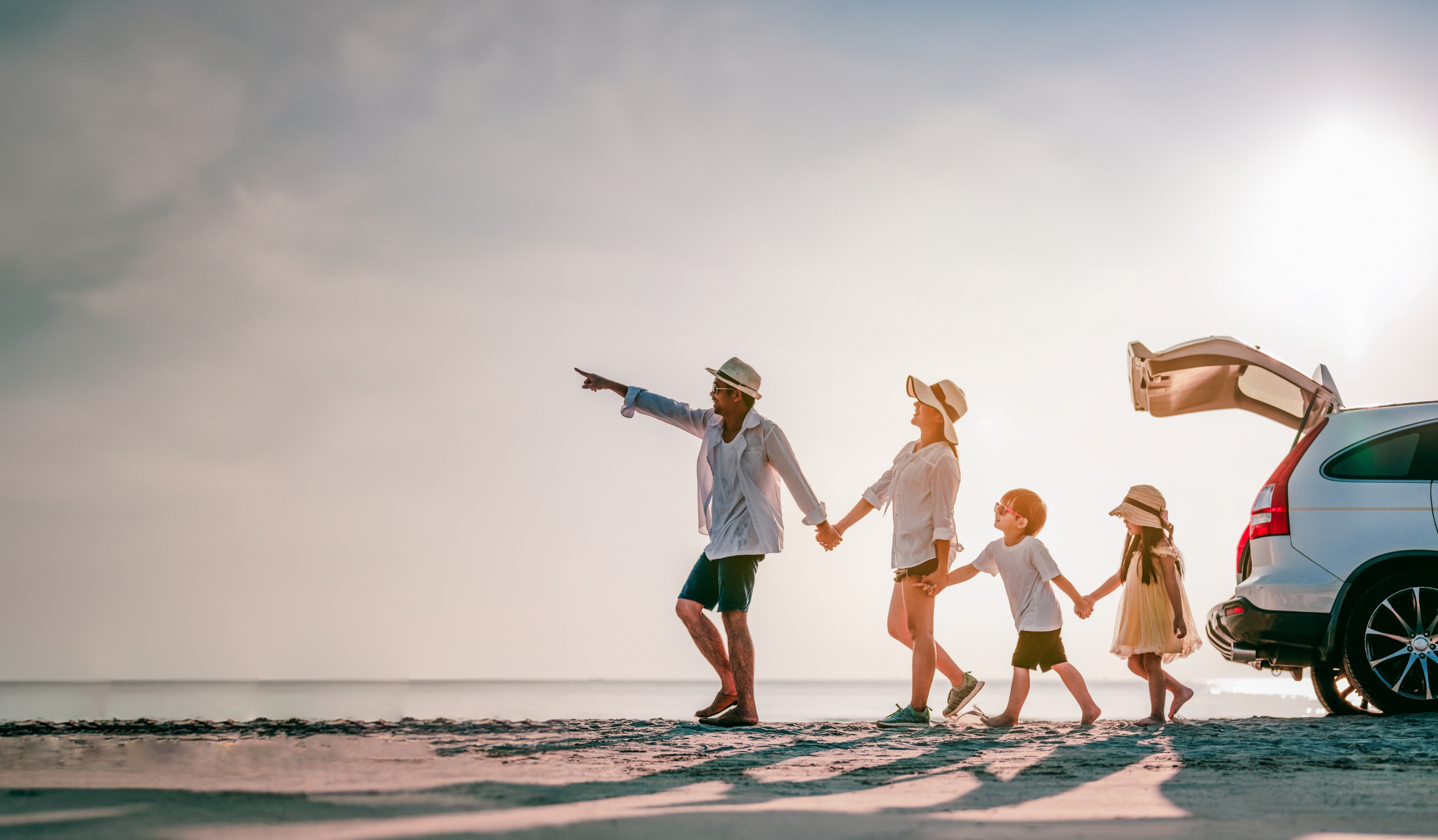 A family walking on the beach with their car parked nearby and the trunk open